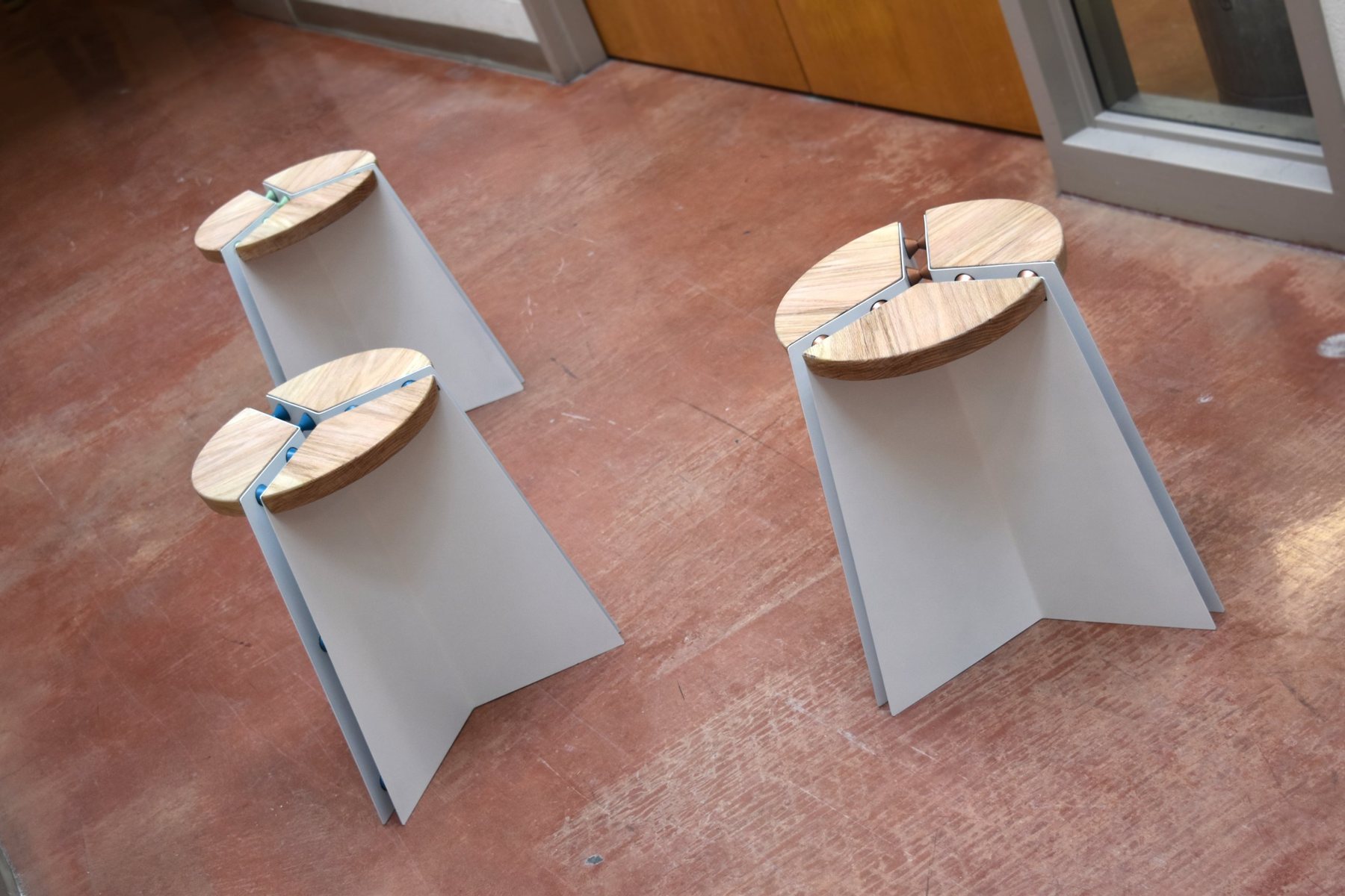 Three finished stools with green, blue and copper spacers on a terracotta floor