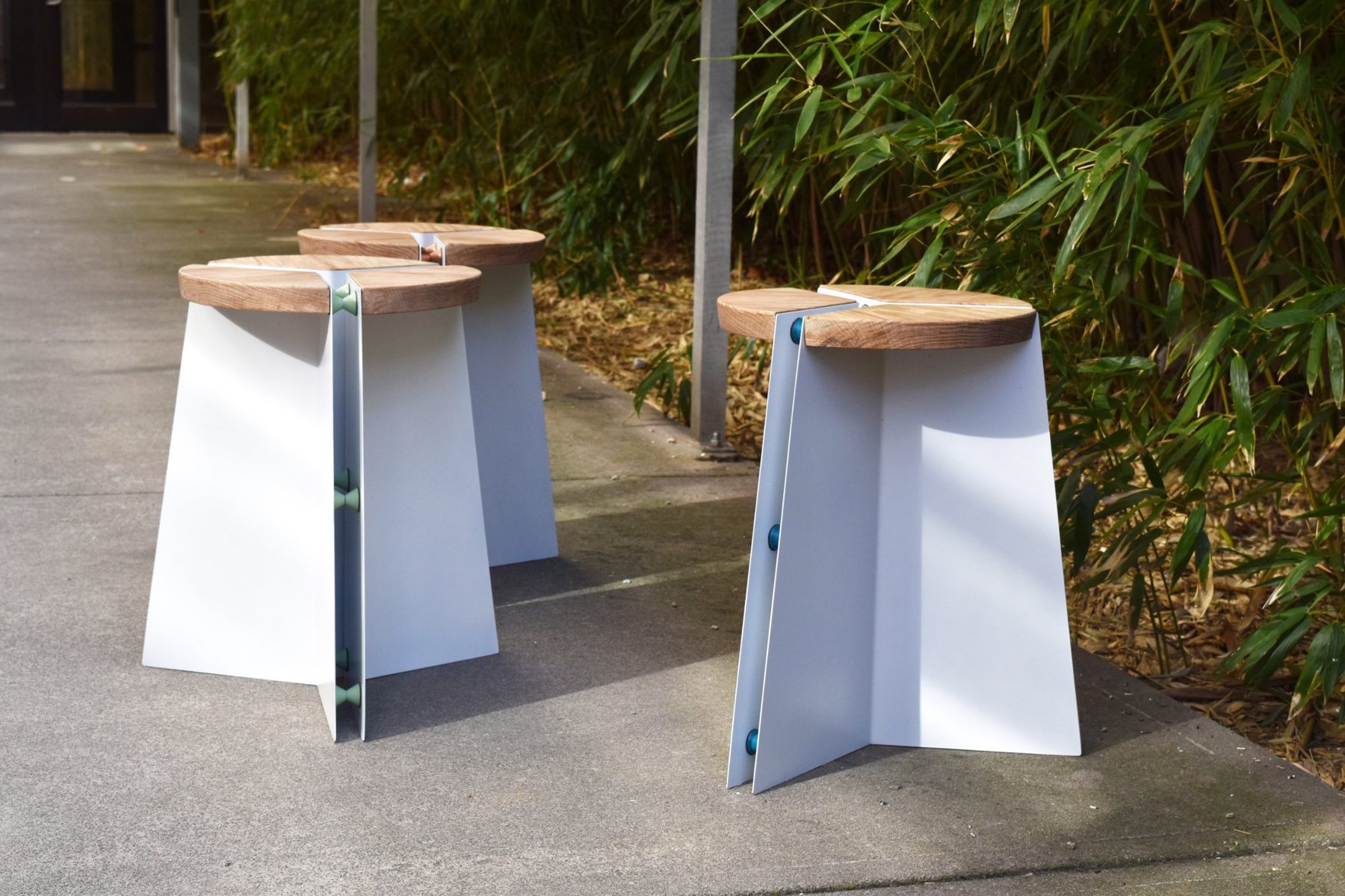 Three Almaz stools with green, copper and blue spacers outside beside bamboo