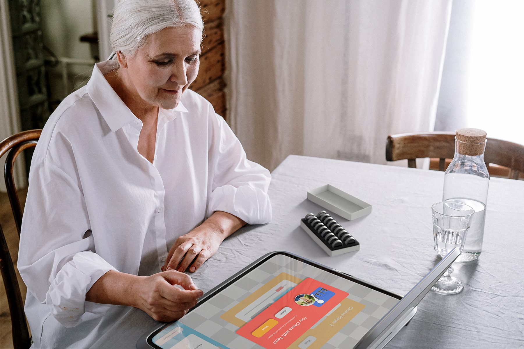 Older woman starting a chess game on the Amity console at her dining table