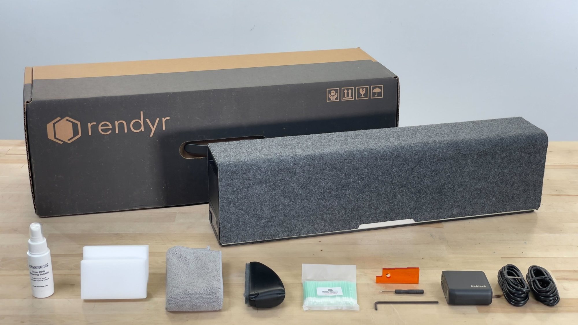 Optic box with the folded Optic and its accessories laid out in front: cleaning spray, sponge, cloth, mat brush, swabs, height gauge, tools, power supply and cables